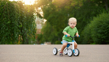 Cute little baby boy rides a balance bike in a summer park. Child learning to ride a bicycle
