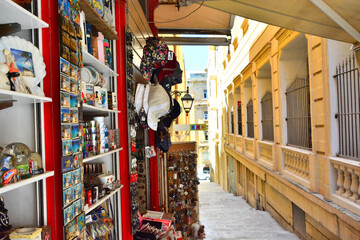 Souvenir shop in narrow street with historic sand-colored houses in capital city of Valletta, Malta
