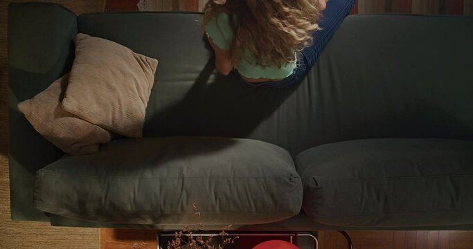 Young woman waking up from nap getting up from couch. From above angle of millennial girl gets up after rest