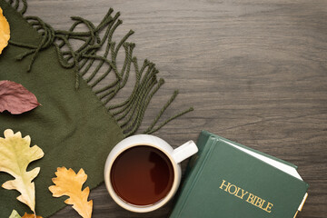 Bible and cup of coffee with autumn leaves and green blanket on a dark wood table with copy space