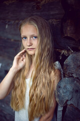 Obraz premium portrait of a beautiful village girl blonde with long hair in a dress and hat sitting by a wooden old barn in summer.