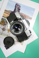 Antique, analog, black and silver photo camera on a turquoise table and printed travel photos - Travel - Lifestyle