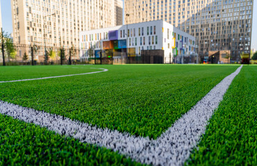 Green synthetic artificial grass soccer sports field with white corner stripe line next to modern school building at background