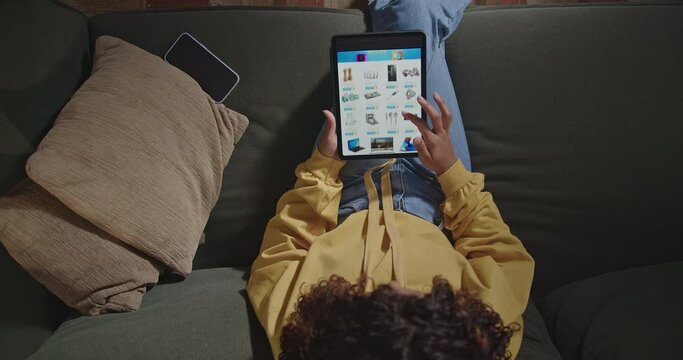 Woman holds tablet surfs online shopping sites. Girl sitting on couch browsing online retail store searching for product to buy