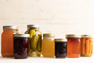 jars of preserved fruits and vegetables lined up up a bright white background with copy space