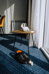 Wedding details, accessories on a wooden table, floor in the morning near the window: bride's shoes, men's belt, groom's boutonniere, gold rings, glass box, garter. Festive photo.