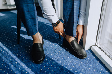 A man, a businessman, is going to work putting black shoes on his feet, sitting on a chair.