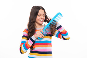 Child brushing combing hair with big comb on white isolated studio background. Teen girl with hairbrush. Kids hairstyle. Happy girl face, positive and smiling emotions.