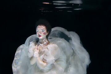 young woman in long white luxury dress underwater on the black background. Motion, art, winter...