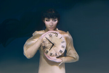 Spooky woman with clock in her hands in black veil underwater