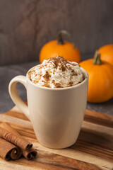 Autumn pumpkin spice latte with cream in mug on dark table. Traditional Coffee Drink for Autumn Holidays. A table decorated with pumpkins. Thanksgiving. Fall time. Vertical orientation. 