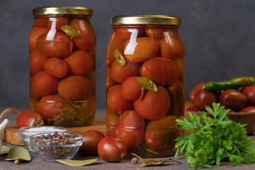 Fototapeta na wymiar Homemade pickled tomatoes with chili peppers and parsley in two jars on gray background, front view