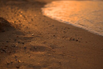 The sandy shore of the Sea of Azov at sunset, a warm summer evening, the waves are beating against the shore, stroking the sand with sea foam, defocus, selective focus.