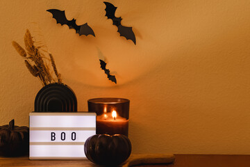 Halloween decor composition with candle, black pumpkin, bats and light box with text boo