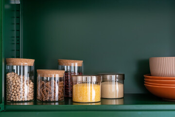 glass containers with grains and pasta on shelf in kitchen cupboard