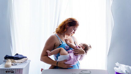 Mother breastfeeding baby near window