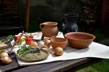 Obraz na płótnie Canvas A view of a wooden table full of medieval style dishes and condiments including carrots, ground pepper, basil, thyme, rice, flour, and many other foodstuffs seen on a sunny summer day in a garden