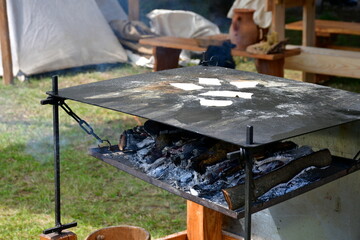 A close up on a simple cooking plate with some smoking logs beneath it used to cook shortbread and other delicacies during a medieval fair seen on a sunny summer day in Poland
