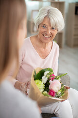 beautiful adult woman is giving flowers to her mature mother
