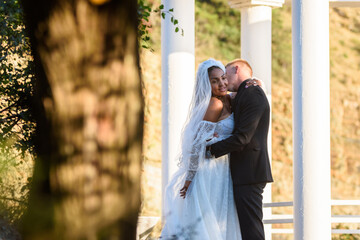 Young beautiful interracial newlyweds hugging against the background of white columns