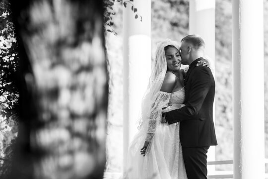 Portrait of interracial newlyweds hugging against the background of columns, black and white photography