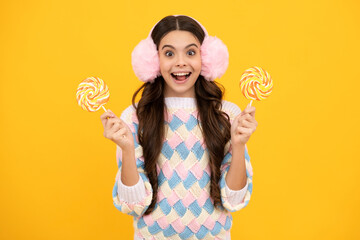 Funny child with lollipop over yellow isolated background. Sweet childhood life. Teen girl with yummy caramel lollipop, candy shop. Teenager with sweet sucker.