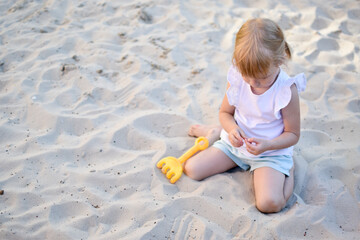 The girl is sitting and playing in the sandbox. Modern playground. Active recreation in the city