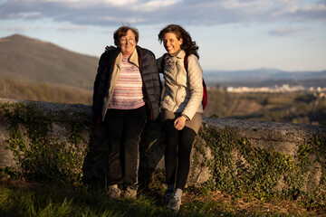 Adult Daughter Sitting on a Church Wall with Senior Mother Serene Talking at Sunset