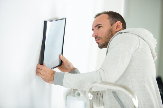 portrait of man hanging blank picture on wall