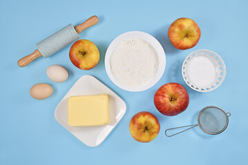 Fototapeta na wymiar Baking ingredients for apple pie with butter, flour, sugar, eggs and fruits on blue background