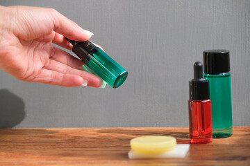 hand with bottle of serum next to cosmetic bottles and soaps on wooden surface agains gray wall, closeup 