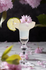 Spring still life with a glass of cold Margarita with lime, pink sakura flowers 