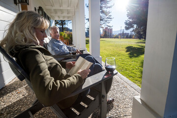 An elderly woman reads and enjoys a glass of wine with her husband.