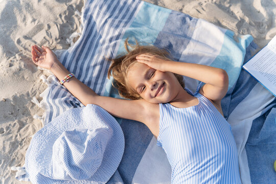 A girl on the beach is resting on a towel and smiling.