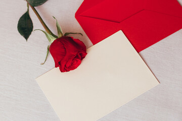 Red rose and envelope with copy space, laying on white bed. Valentine's day background, love and romance.