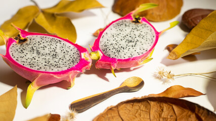 AUTUMN, DRAGON FRUIT, PITAHAYA WITH RED SKIN AND WHITE PULP ON WHITE BACKGROUND WITH DRY LEAVES