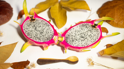 AUTUMN, DRAGON FRUIT, PITAHAYA WITH RED SKIN AND WHITE PULP ON WHITE BACKGROUND WITH DRY LEAVES