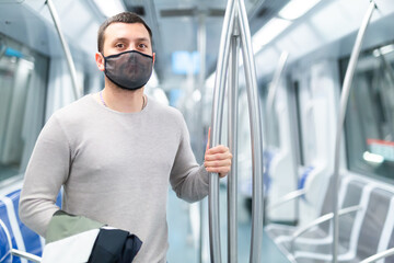 Young passenger in protective face mask holding on to handrails while riding in subway car. Concept...