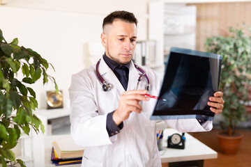 Fototapeta premium European man physician standing in office and analyzing roentgenogram.