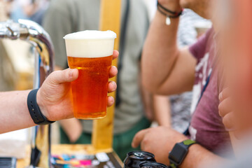 The hand holds a plastic glass with beer.