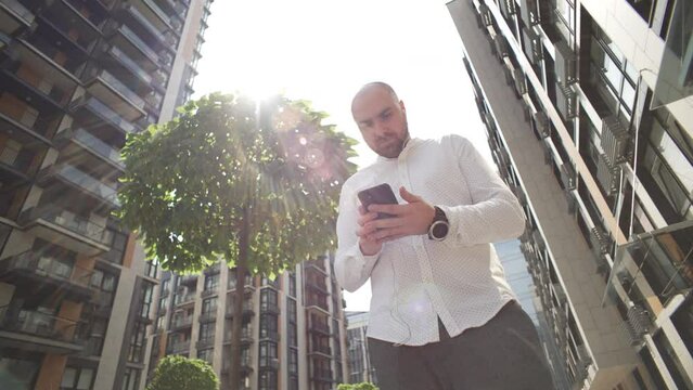 A businessman is texting on the phone near the business center. A serious expression of enthusiasm and concentration, a person conducts negotiations and responds to work emails. High quality 4k 