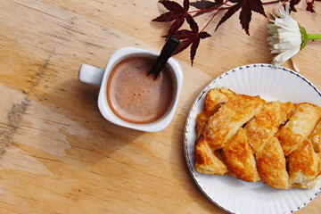 Coffee mugs and pastries served on a wooden table with crimson Japanese maple leaves and white daisies. Top view photo.