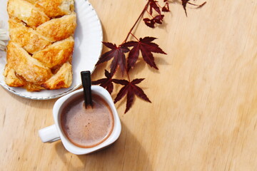 Coffee mugs and pastries served on a wooden table with crimson Japanese maple leaves and white daisies. Top view photo.