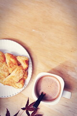 Coffee mugs and pastries served on a wooden table with crimson Japanese maple leaves and white daisies. Top view photo.