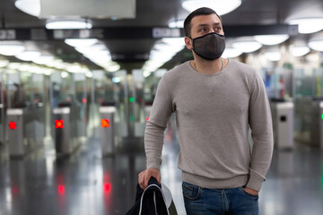 Focused young traveler in black protective mask waiting for subway train, walking at modern...