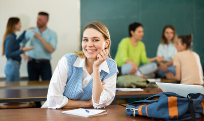 Portrait of a student girl sitting at desk with a pen and a copybook during a study break, preparing for classes in the ..university auditorium