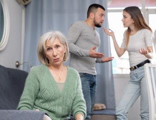 Displeased senior woman waiting for her adult son and daughter-in-law to calm down and stop quarreling at home