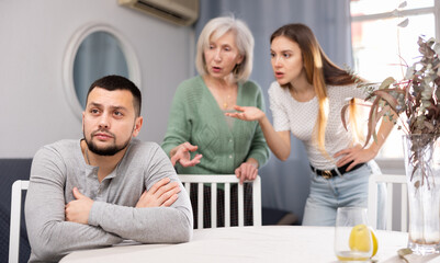 Man ignoring his wife and mother-in-law standing behind and arguing with him at home.