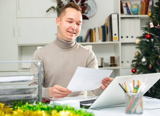 Cheerful man bookkeeper doing paperwork in his workplace in office. Smiling office manager working during Christmastime.