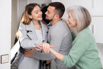 Happy man and mature women joyfully greeting and embracing young woman returned home at doorway